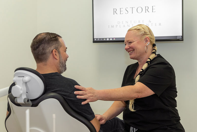 treatment coordinator smiling at matthew, full arch dental implant patient, in exam chair